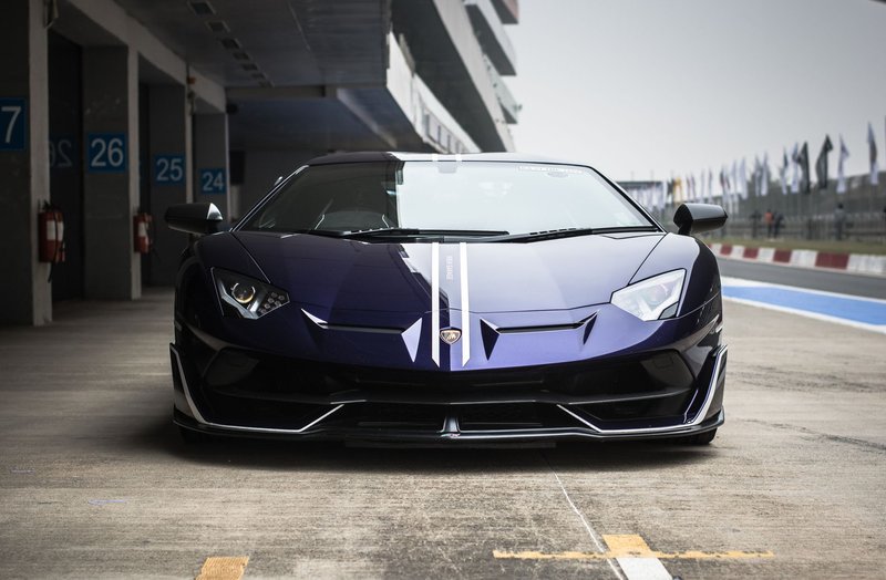 Front view of a shiny black Lamborghini Aventador parked on a racing track, showcasing its impressive design.