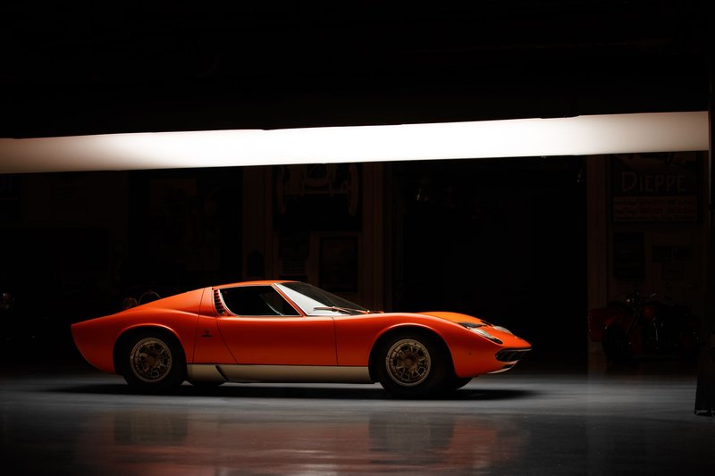 Side profile of a vintage Lamborghini Miura under studio lights, showcasing its retro design.