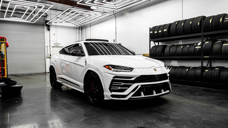 White Lamborghini Urus parked in a stylish garage with stacked tires and modern lighting.
