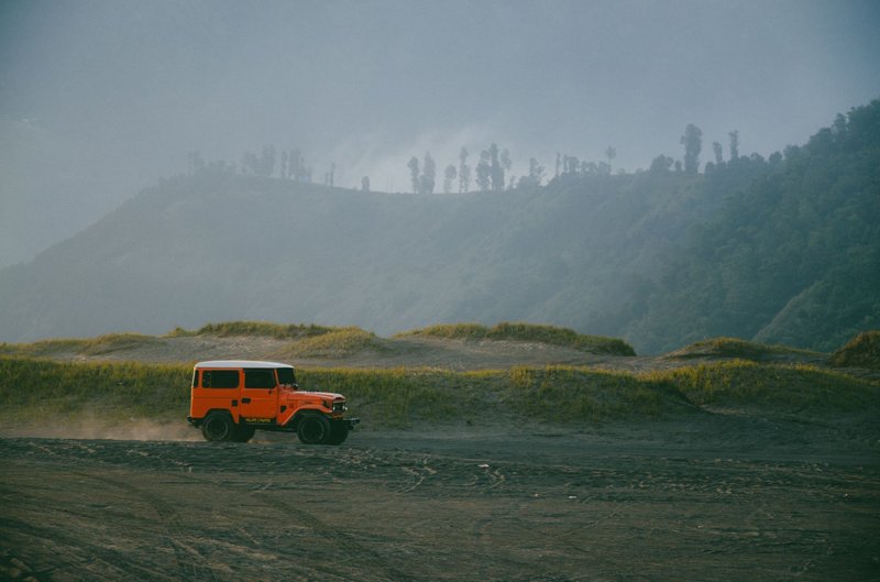 Orange SUV traversing a dirt road in the scenic mountains of East Java, Indonesia.