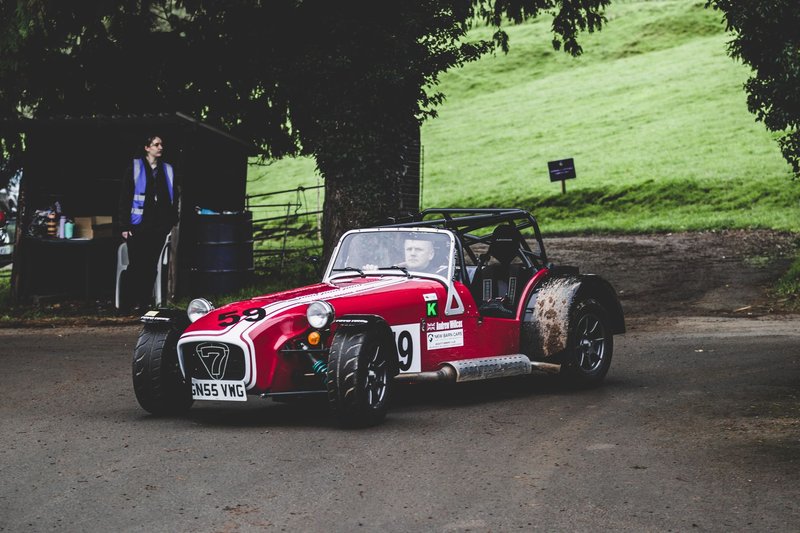 A vibrant red Caterham Seven sports car parked on a rural race track during the day.