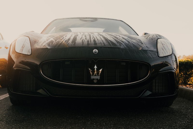 Front view of a sleek black Maserati with raindrops on the hood in a parking lot.