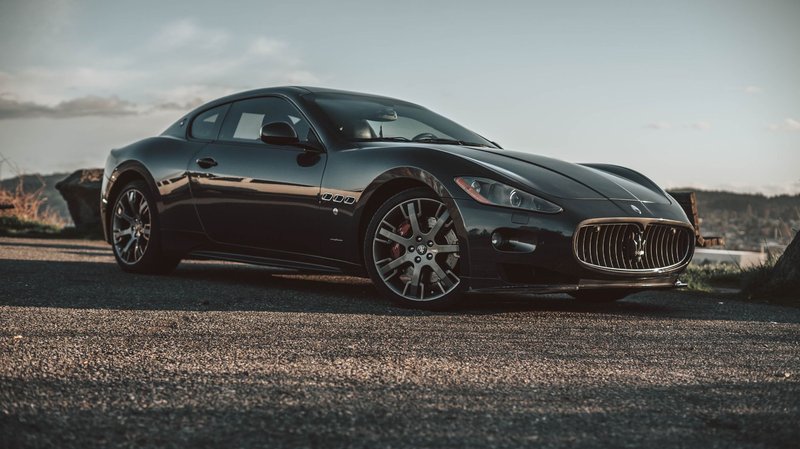Luxurious black Maserati captured on an open road at sunset, highlighting its elegant design.
