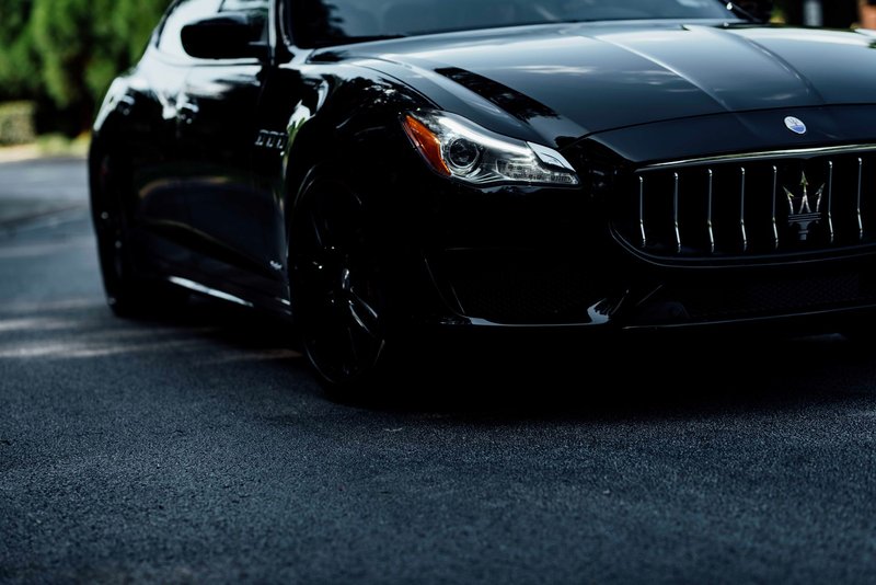 Close-up of a sleek black Maserati Quattroporte on a road, embodying luxury and elegance.