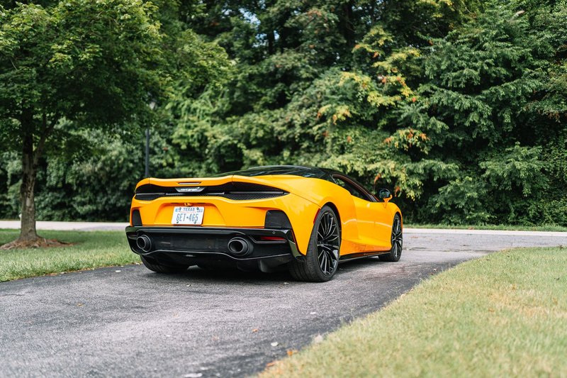 A stunning yellow sports car parked on a driveway with lush green trees in the background.