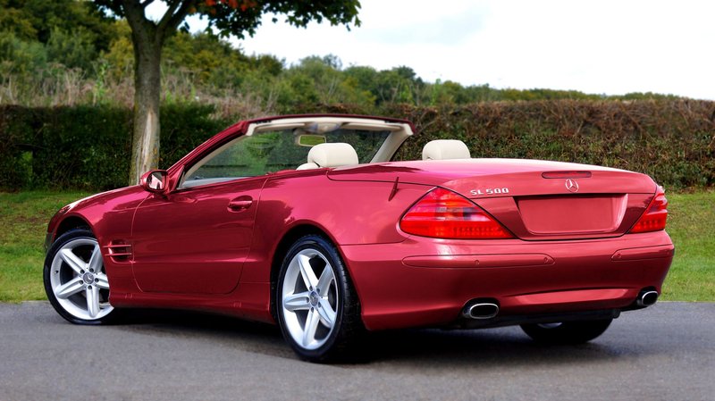 Shiny red Mercedes SL500 convertible parked outdoors, showcasing luxury design and elegance.