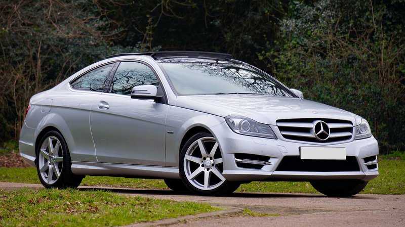 A sleek silver Mercedes-Benz coupe parked on a quiet, scenic road surrounded by greenery.