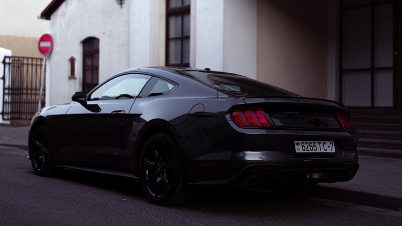 A sleek black Ford Mustang parked on an urban street near buildings and sidewalks.