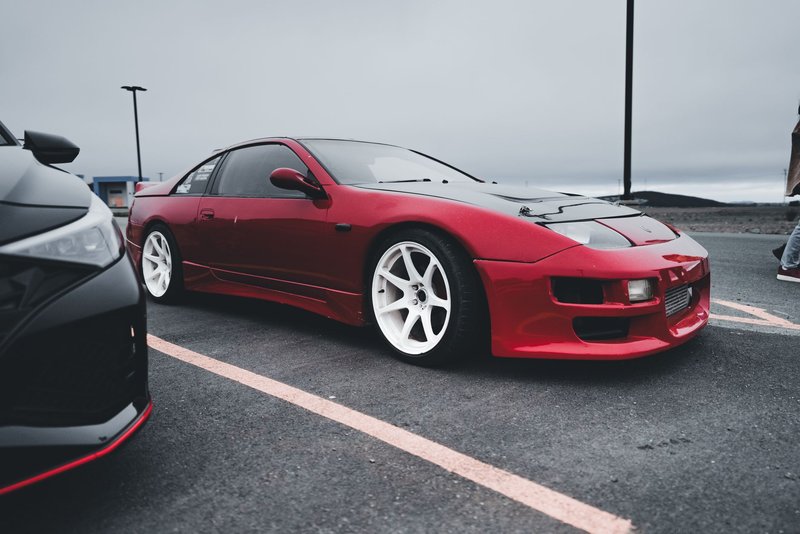Close-up of a red Nissan sports car with custom white rims parked on an asphalt lot.