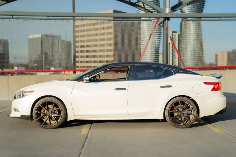 White Nissan Maxima parked on a rooftop in Mississauga, Ontario with city skyline view.
