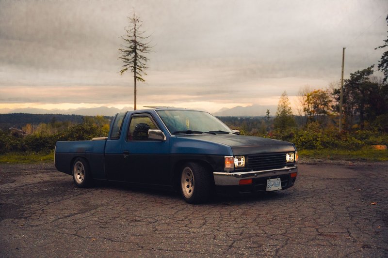 A modified Nissan pickup truck parked against a scenic autumn backdrop with mountains in view.