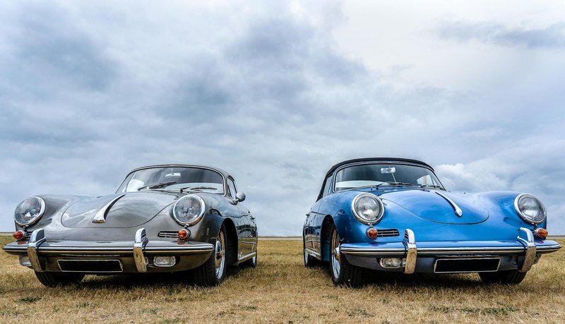 Two vintage classic cars showcased outdoors on a cloudy day, highlighting their timeless design.