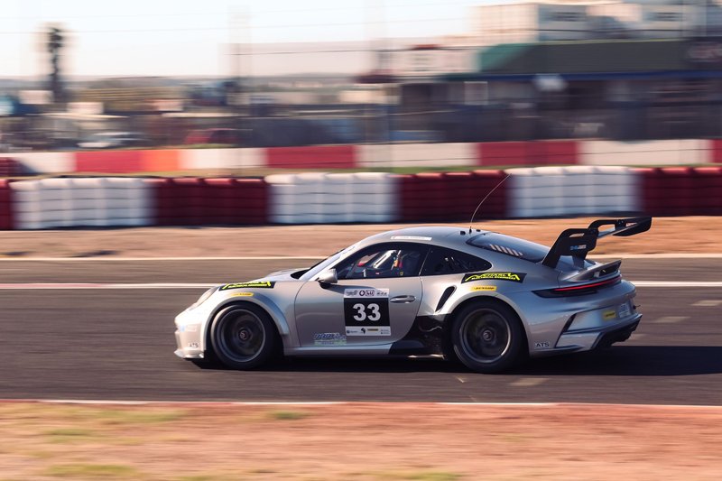 Dynamic shot of a silver race car speeding on a track at sunset, capturing motion and speed.