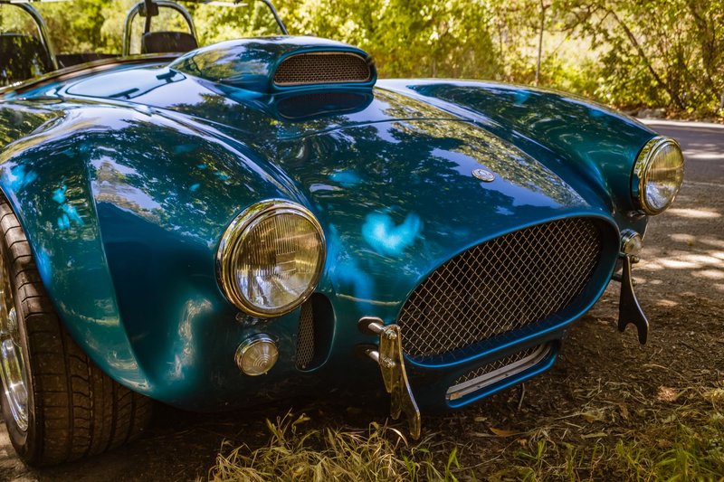 A vintage Shelby Cobra sports car parked outdoors in a scenic setting.
