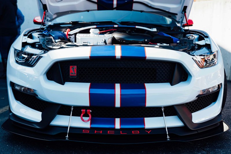 Close-up of a Ford Mustang Shelby GT350 with hood open, showcasing its powerful engine at a car show.