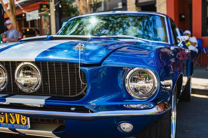 Close-up of a vintage blue Ford Mustang with white stripes at an outdoor car show, capturing its classic design.