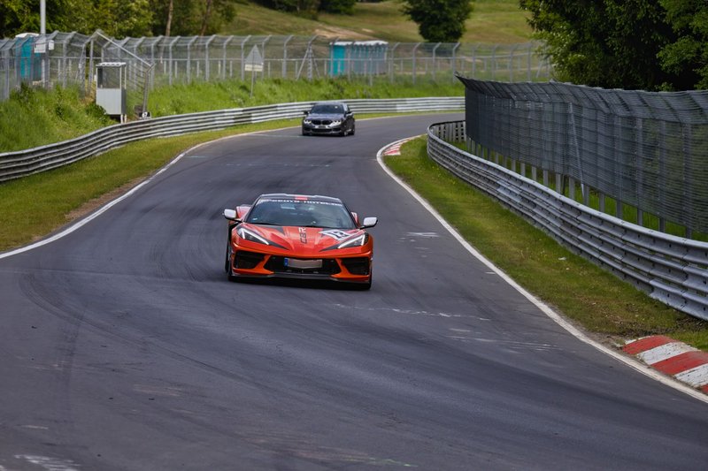 Dynamic car racing scene on a famous European race track amidst lush greenery.