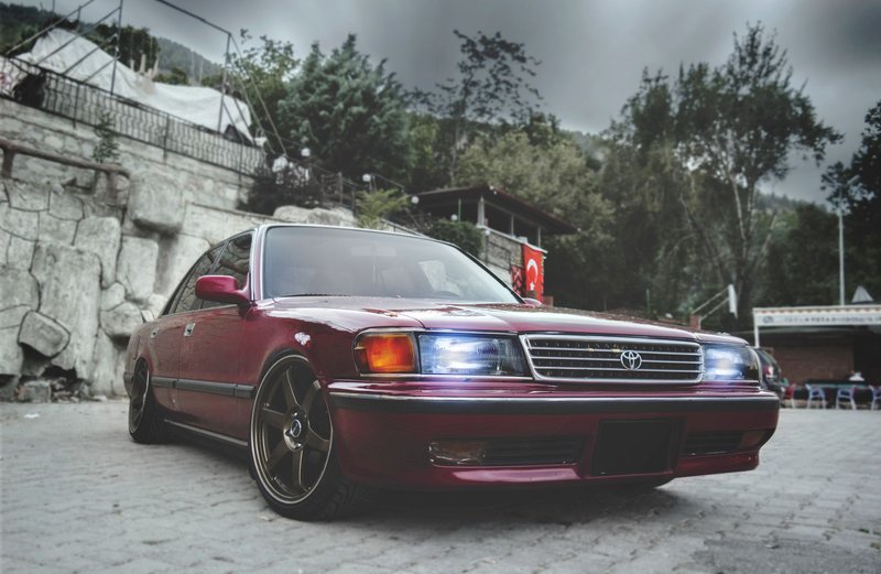A classic luxury sedan with bright headlights parked on a paved outdoor area.