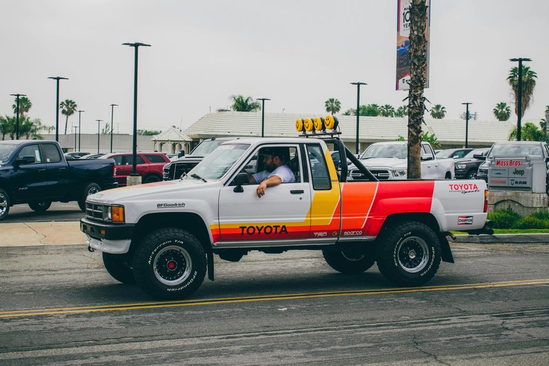A classic Toyota pickup truck with retro decals at an outdoor car meet. Vibrant colors and iconic design.