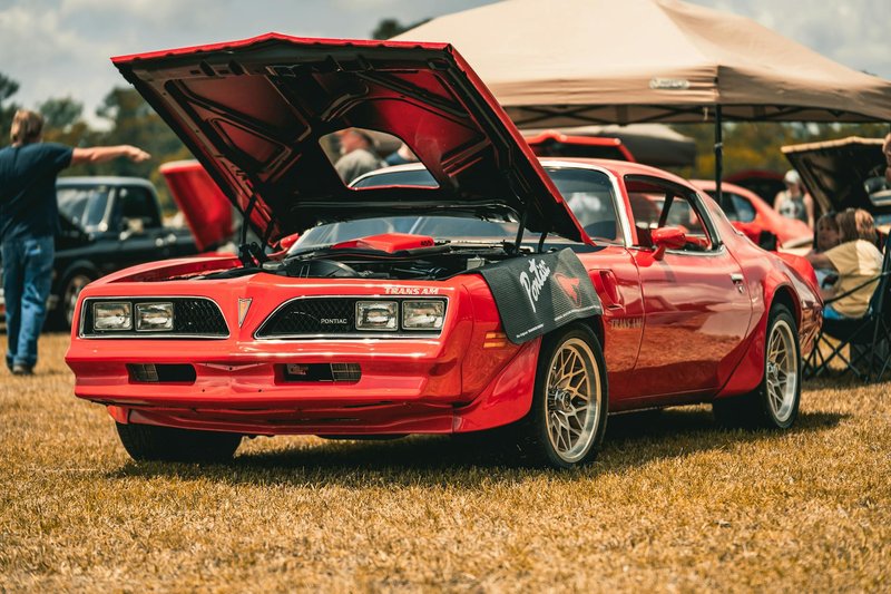 Vintage red Pontiac Trans Am with hood open on display at an outdoor car show.