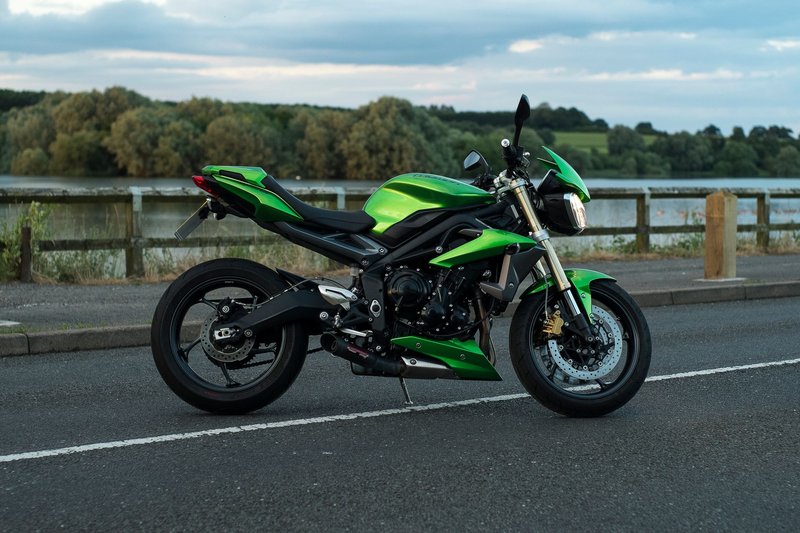 A sleek green motorcycle parked on a serene lakeside road during the day.