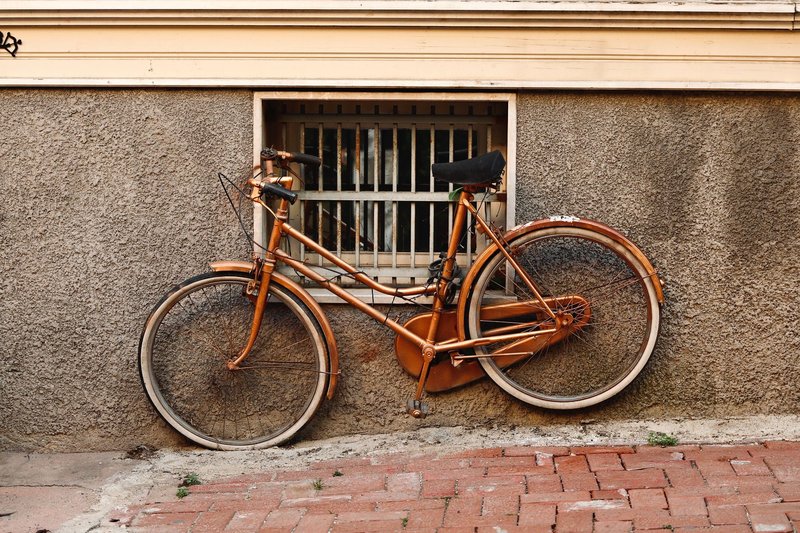 A vintage rusty bicycle leaning against a weathered urban wall with a barred window.