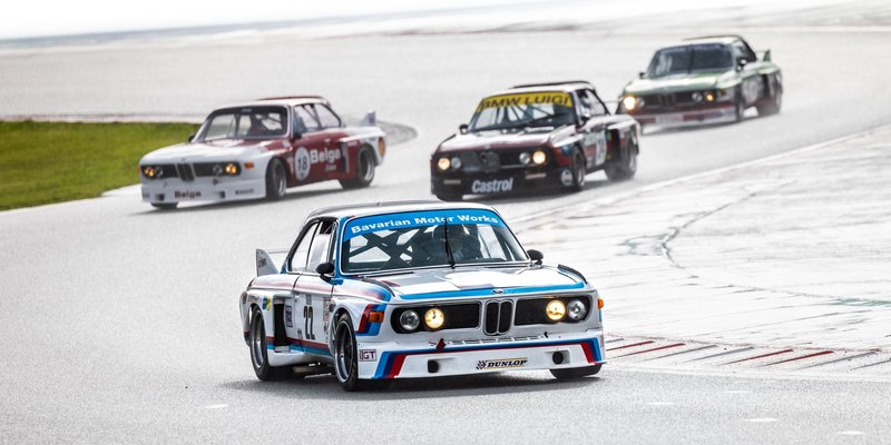 Iconic BMW race cars navigating through a wet racing track showcasing vintage motorsport action.