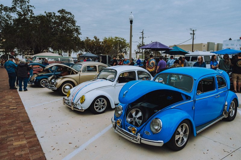 Showcase of colorful vintage Volkswagen Beetles at an urban classic car event.