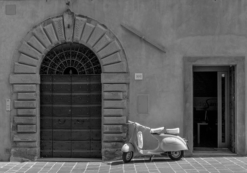 Vintage Vespa parked beside an ornate entrance in a European cityscape, monochrome tone.