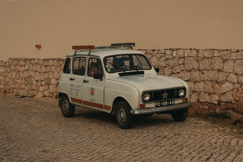 Classic white Renault parked on cobblestone street against a stone wall, exuding vintage charm.