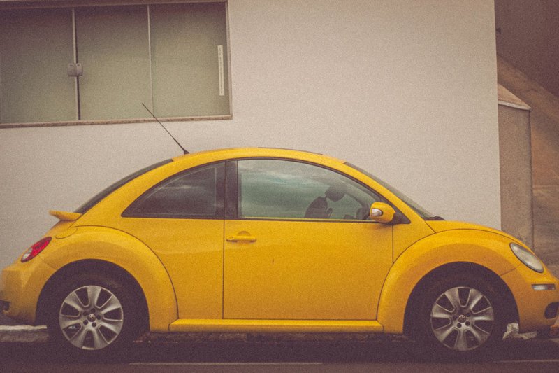 Side view of a yellow Volkswagen Beetle parked beside a building.