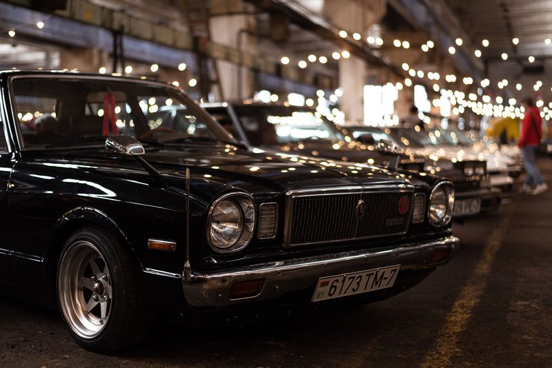 A vintage black Toyota on display at an indoor car show with bokeh lights.