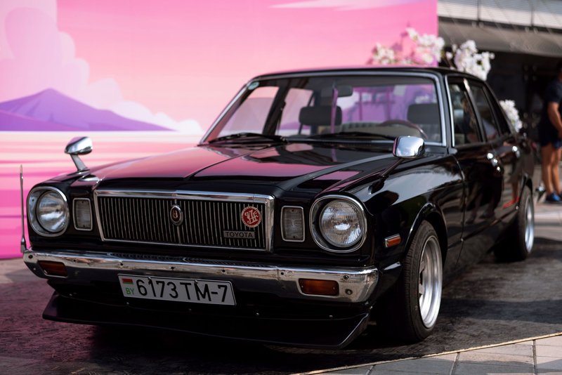 Black vintage Toyota car with retro design showcased outdoors against a colorful backdrop.