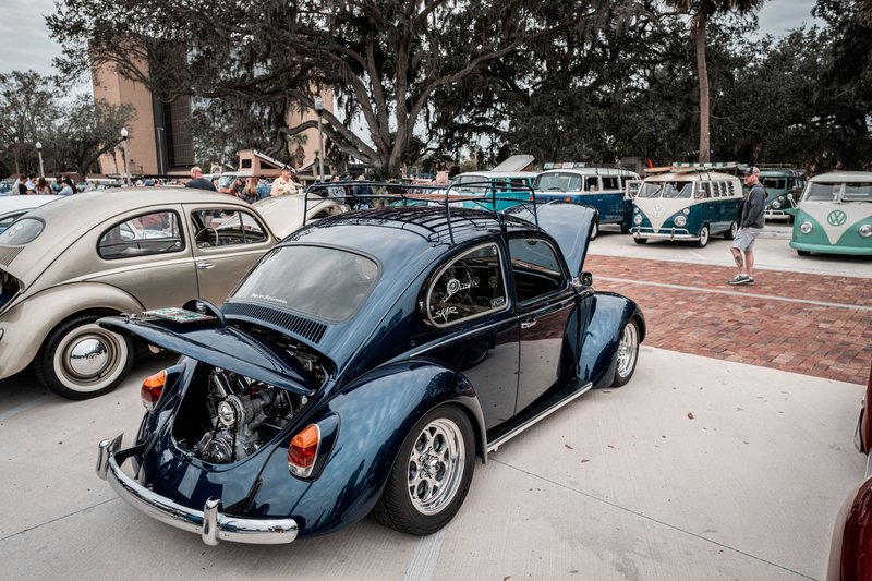 A vintage Volkswagen Beetle with an open trunk showcased at a classic car show outdoors.