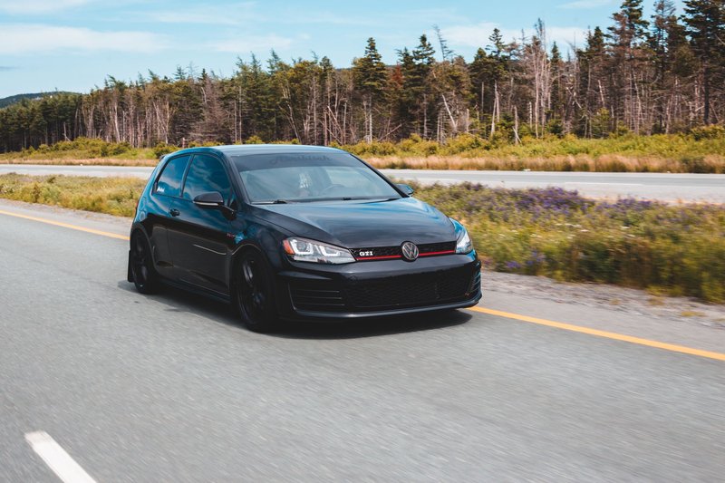 Modern sports car with tuning front bumper going down asphalt road alongside woods