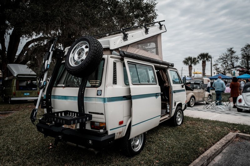 Classic Volkswagen camper van displayed at an outdoor car show with other vintage vehicles.