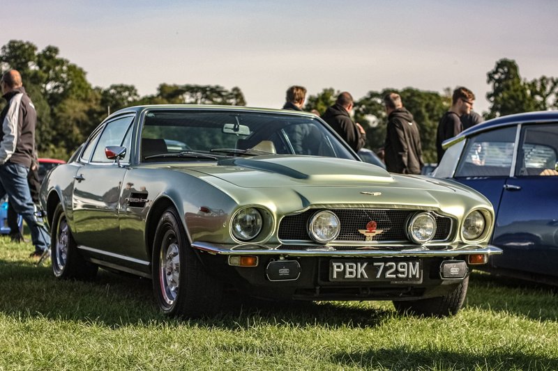 Vintage Aston Martin showcased at a public car show outdoors, surrounded by enthusiasts.