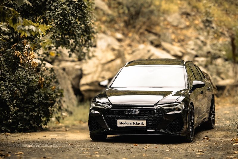 Sleek black luxury car against a natural autumn backdrop, showcasing elegance and design.
