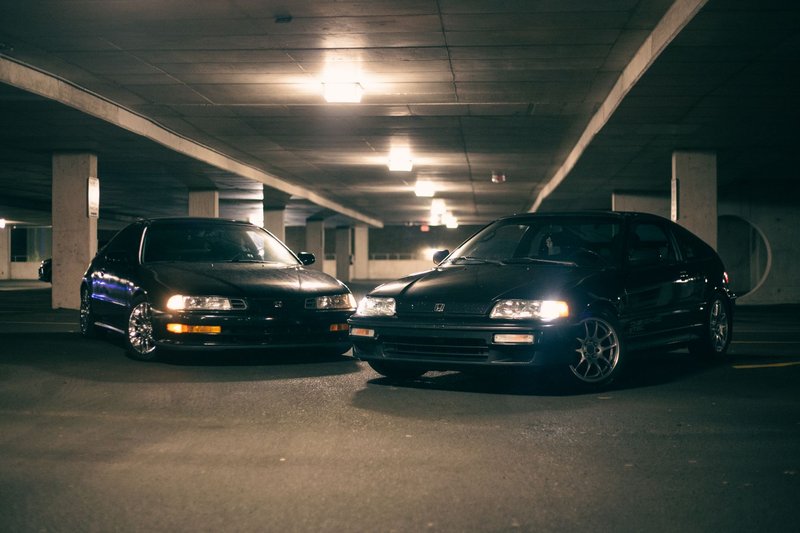 Two vintage Honda cars parked in a dimly lit indoor garage at night, showcasing a classic automotive scene.