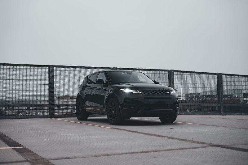 Sleek black SUV parked alone on rooftop with city skyline background.