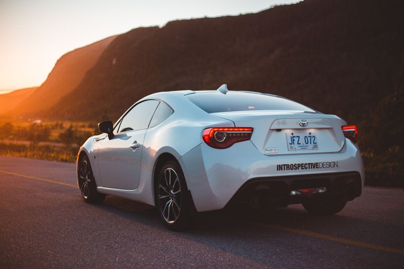 Trendy expensive sport automobile on asphalt route against mountains in valley glowing with sunset light
