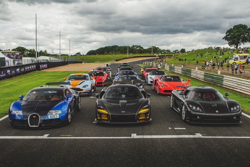A lineup of luxury sports cars ready for a racing event at an outdoor track.