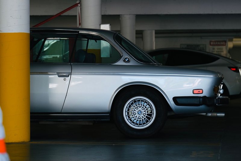 Vintage BMW E9 in a dimly lit urban parking lot with yellow pillars.