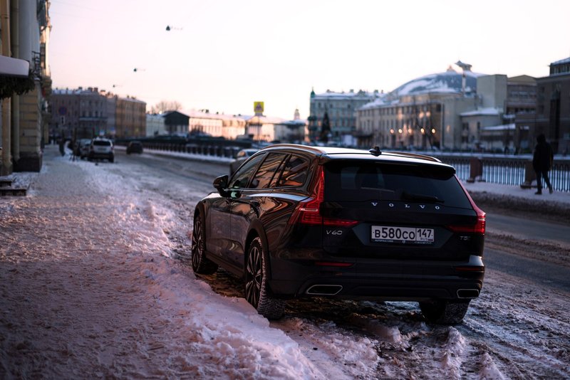 Black Volvo V60 parked on a snow-covered street in a winter city scene at sunset.