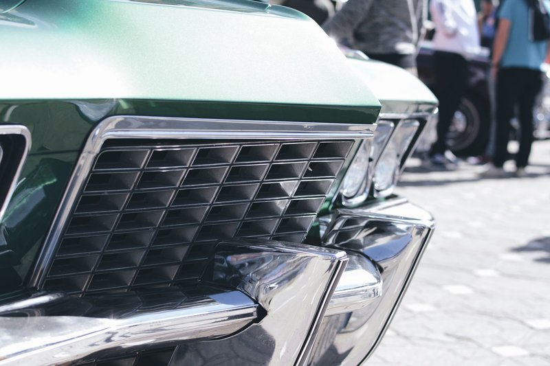 Vintage car grille close-up with shiny chrome details at an outdoor auto show.