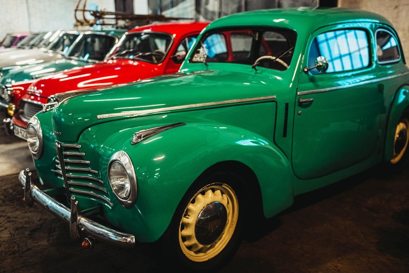 Collection of classic vintage cars parked in an indoor garage setting, showcasing vibrant colored vehicles.
