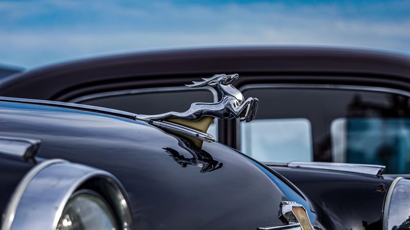 Close-up of a classic vintage car hood ornament against a clear blue sky, showcasing elegance and design.