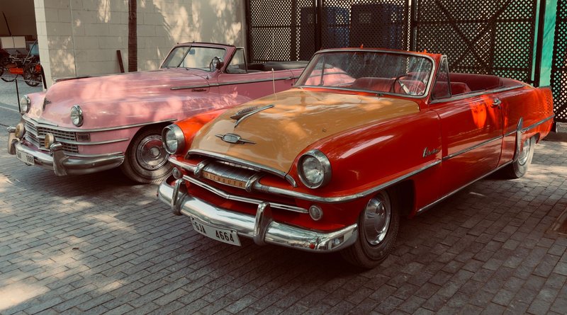 Classic vintage convertibles featuring vibrant colors parked outdoors on a sunny day.