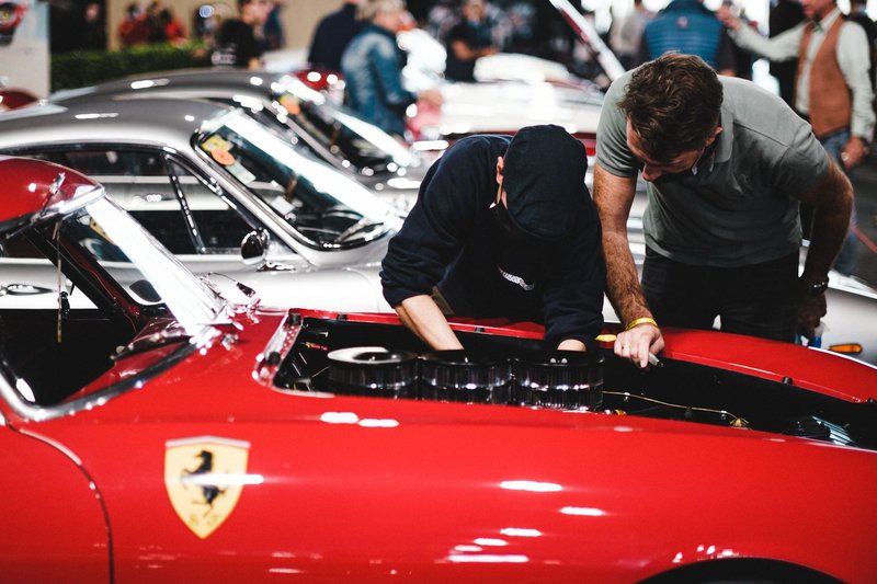 Red Ferrari with mechanics inspecting engine at a classic car show.