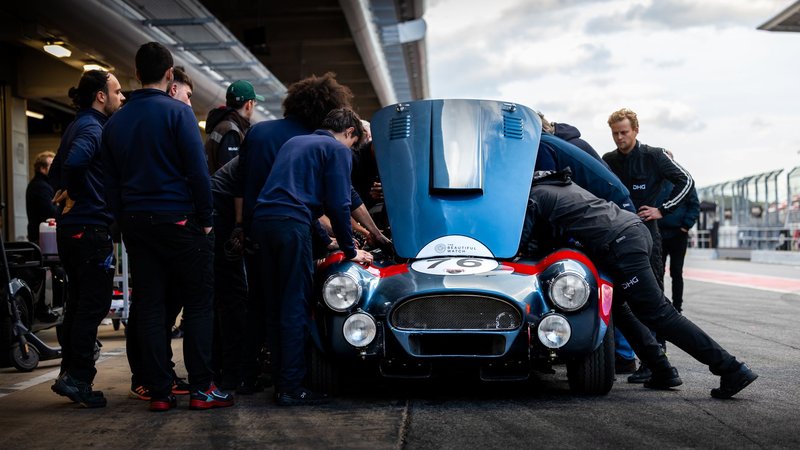 Engineers perform maintenance on a classic race car in the pit lane, showcasing teamwork and dedication.
